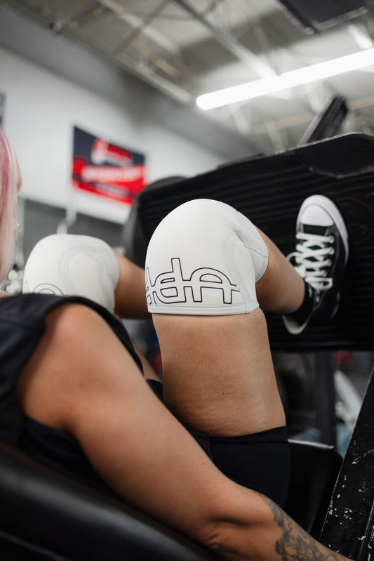 woman using leg press machine with uppper knee sleeves white